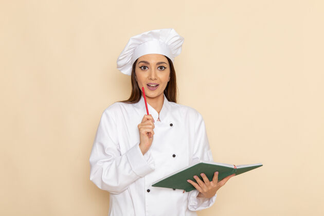烹饪身穿白色厨师服的年轻女厨师正拿着浅白色墙上的绿色抄写本女性工作医生