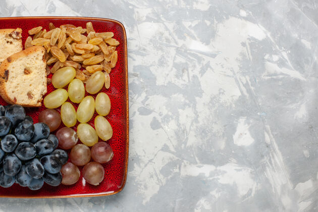 葡萄顶视图蛋糕片与葡萄和葡萄干内红色盘子上的白色表面蛋糕素食者橄榄