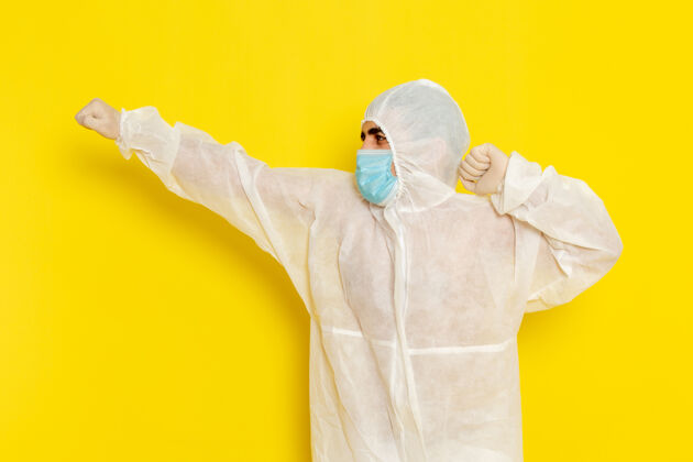 危险身穿特殊防护服 戴着面罩的男科学工作者正对着淡黄色的墙上摆姿势保护科学健康