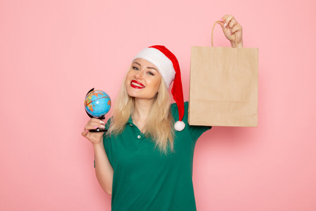 圣诞正面图年轻女性手持地球仪和粉红色墙上的圣诞礼物照片模型圣诞节新年假期肖像地球美丽