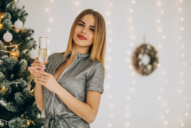 事件在圣诞树旁和香槟一起的年轻女人快乐成人积极