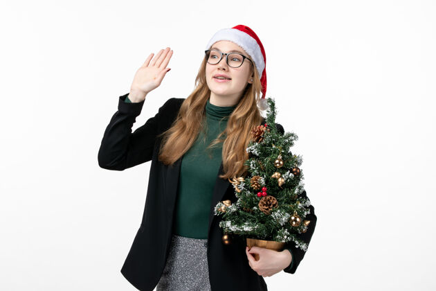 成人正面图年轻女性手持圣诞树在白色墙上新年圣诞玩具肖像风景年轻女性