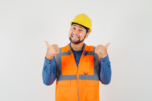 工程师年轻的建筑工人在衬衫 背心 头盔上竖起大拇指 看上去很高兴 正面视图建筑肖像安全帽