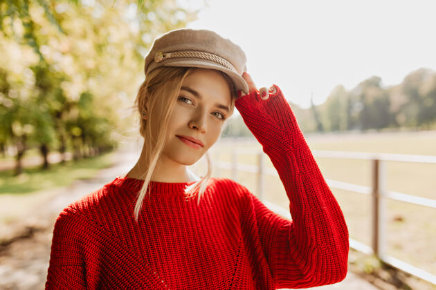 阳光穿着红色套头衫 戴着浅色帽子的迷人年轻女子在公园里看起来不错美丽的金发女郎在秋天穿着漂亮的配饰和时髦的衣服金发公园热