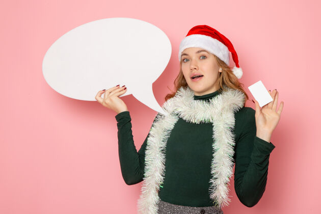 大正面图年轻女性手持白色大招牌和银行卡在粉色墙上的模特节日圣诞新年色彩感慨年轻的女性圣诞节银行