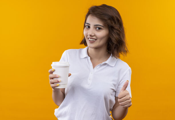 穿短发少女 身穿白色马球衫 端着咖啡杯 兴高采烈地竖起大拇指展示咖啡橙色