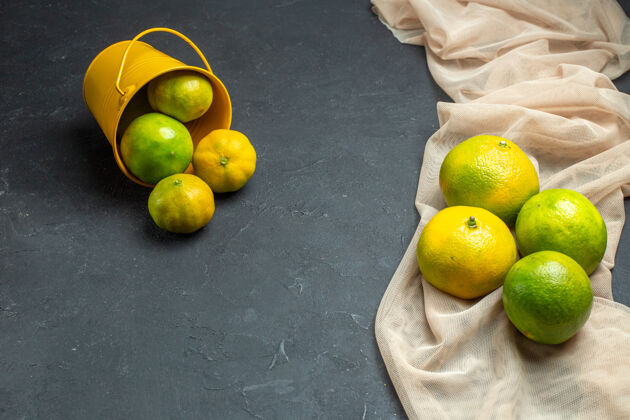 顶部顶视图新鲜柠檬在米色薄纱披肩柠檬从桶里散落在黑暗的表面与复制空间柠檬景观水果