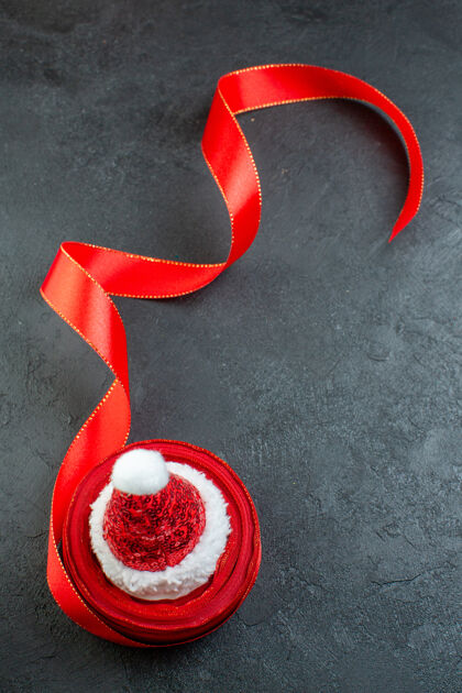 季节一卷红丝带的垂直视图 黑色背景上有圣诞老人的帽子球轮子弓