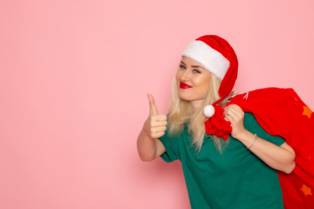 年轻女性正面图：年轻女性提着红包 在粉色墙上放着礼物假日模特圣诞新年彩照圣诞老人颜色风景帽子