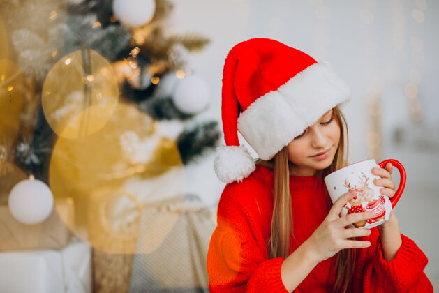 时尚在圣诞树旁喝可可的女孩传统圣诞人