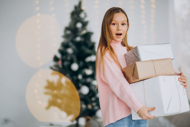 开放可爱的女孩拿着圣诞礼物在圣诞树旁灯乐趣青少年