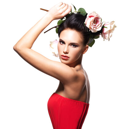 模特身着红色连衣裙 头发上有花朵的美丽年轻女子的肖像——孤立于白色之上女人吸引力玫瑰