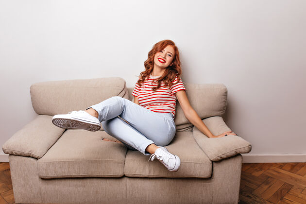 红发穿着胶布鞋的梦幻少女在家拍照时表达幸福穿着休闲牛仔裤的姜汁女孩坐在沙发上美丽情绪沙发