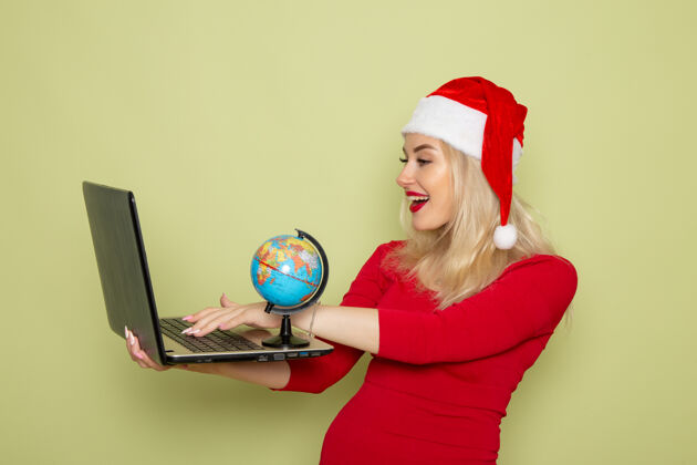 漂亮的女人正面图美丽的女性手持小地球仪和笔记本电脑在绿色的墙上圣诞彩雪新年感慨微笑肖像漂亮