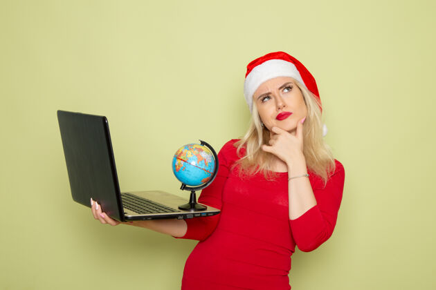 雪正面图美丽的女性手持地球仪 在绿色墙壁上使用笔记本电脑圣诞色雪景新年感慨地球仪圣诞节颜色