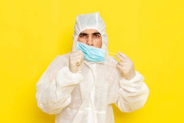 防护身穿特殊防护服的男科学工作者在黄色墙壁上脱下面具的正面图带特殊面罩