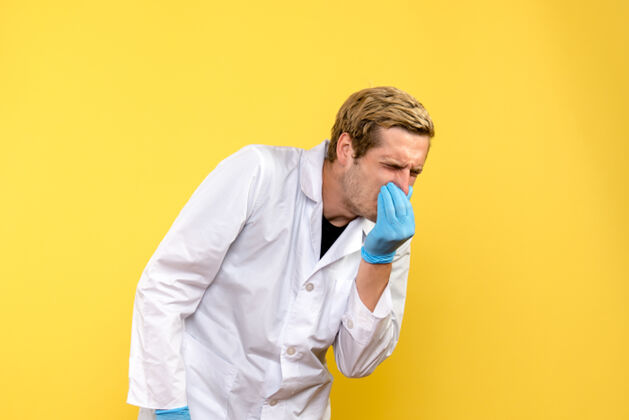 男性前视图男性医生在黄色背景上闭上鼻子人类医学大流行病毒男性医生封闭听诊器