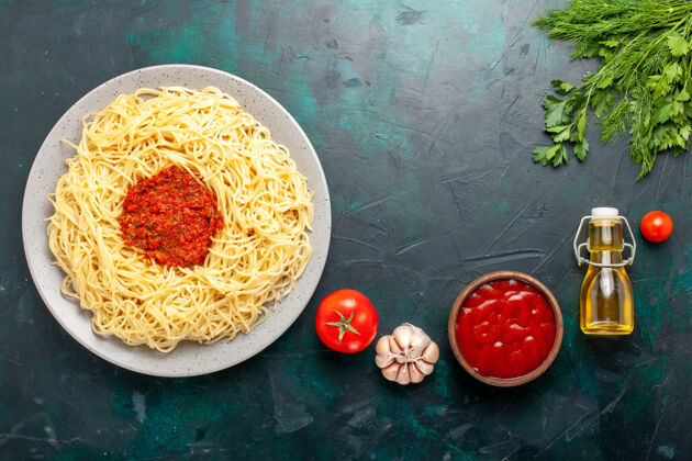 托盘在黑暗的书桌上俯瞰用番茄肉末和油做成的意大利面食碗配料食物