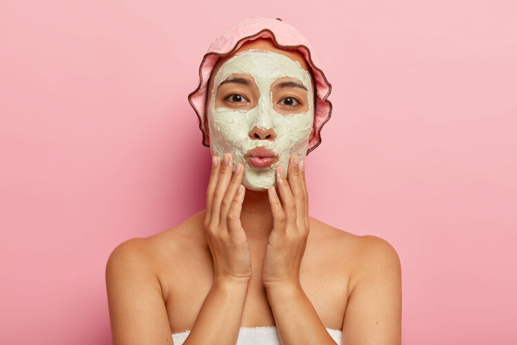 沐浴用可爱的化妆面膜贴近可爱的亚洲女人的肖像 轻轻抚摸脸部 保持嘴唇的折叠 直视 享受清洁和美容护肤品皮肤卫生面部