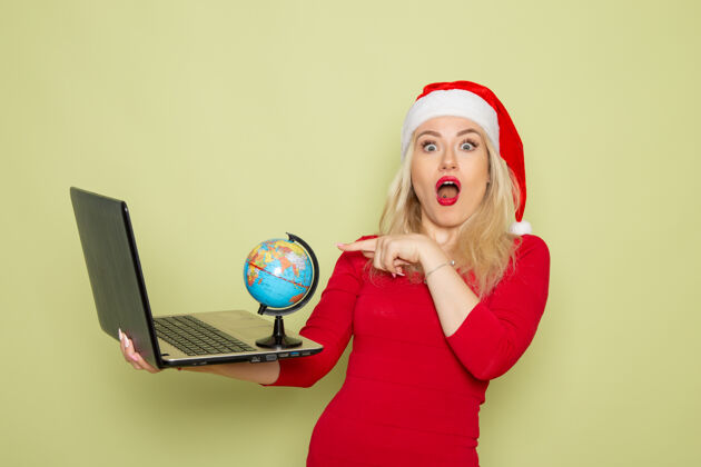 漂亮正面图美女拿着小地球仪 在绿墙上用笔记本电脑圣诞彩雪过年感慨小圣诞节颜色