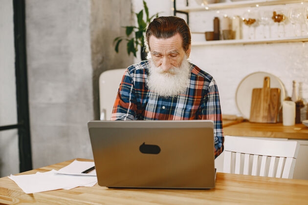 书桌拿着笔记本电脑的老人坐在圣诞装饰品里的爷爷穿手机衫的男人装饰网站通信