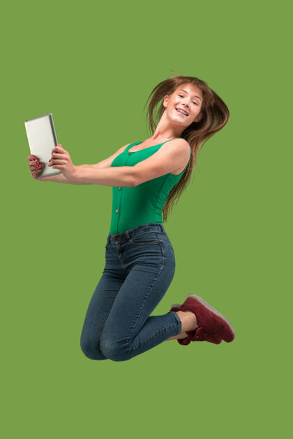 博客年轻女子在跳跃时使用笔记本电脑或平板电脑小工具跳过果岭奔跑的女孩在运动或运动跳跃电脑绿色