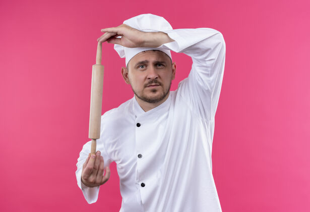 制服年轻帅气的厨师穿着厨师制服 手里拿着擀面杖 看上去孤立在粉色的空间里别针拿着厨师