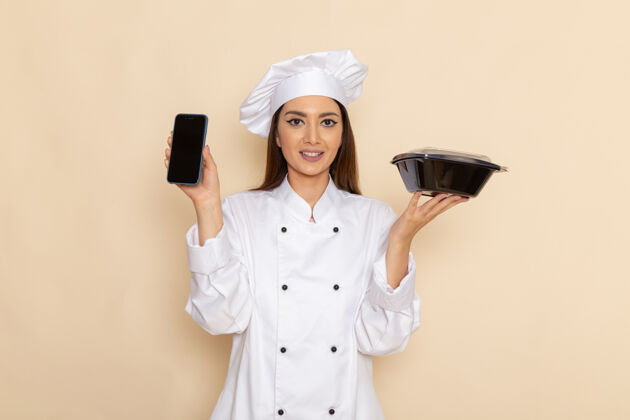 厨房身穿白色厨师服的年轻女厨师正拿着电话和白墙上的黑碗碗制服烹饪