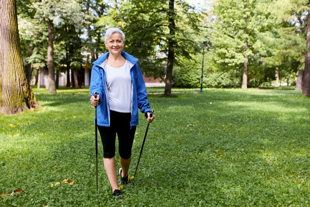 妇女在宁静的夏日早晨 穿着运动服 欣赏美丽野性的时髦开朗的老年妇女 用特制的拐杖行走 带着快乐的笑容运动北欧老年人