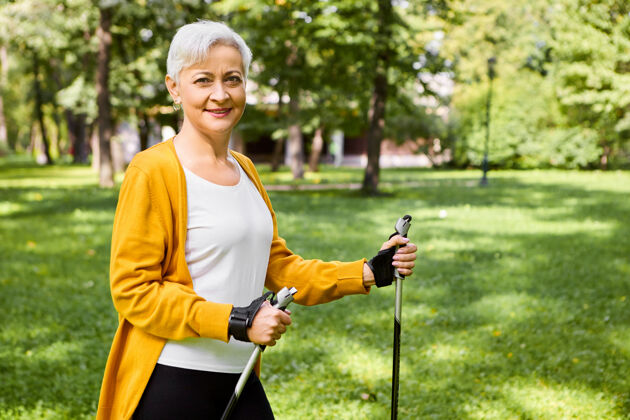 户外图为穿着黄色开衫的美丽快乐的老年成熟女性手持拐杖行走北欧 享受着积极健康的生活方式 感觉精力充沛 笑容可掬北欧人运动活跃