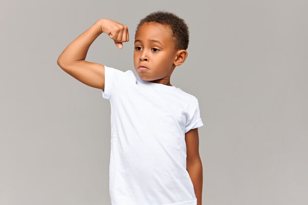 肌肉可爱的深色皮肤的运动型男孩 留着非洲短发 手臂肌肉紧绷 为自己的锻炼感到骄傲自信的酷酷运动型非洲男孩在灰墙展示他的力量男孩展示二头肌