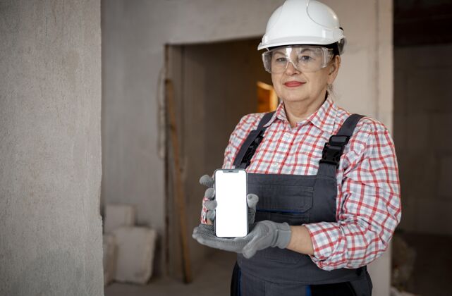 建筑戴着头盔手持智能手机的女建筑工人职业老年人头盔