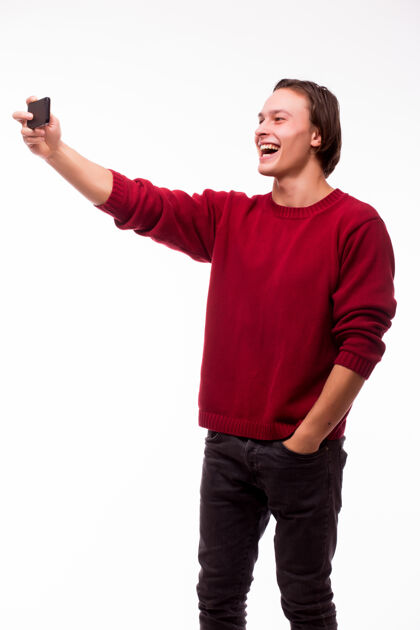 男人快乐的年轻人通过智能手机拍摄自画像隔着白墙电话相机自我