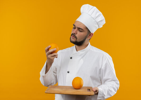 空间体贴的年轻男厨师穿着厨师制服拿着砧板和橘子看着橘子孤立在橘子空间里厨师烹饪思想