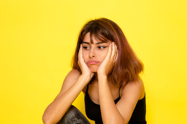 姿势身穿黑色衬衫的年轻女性在浅黄色墙壁上摆出充满压力的姿势情绪模特前面