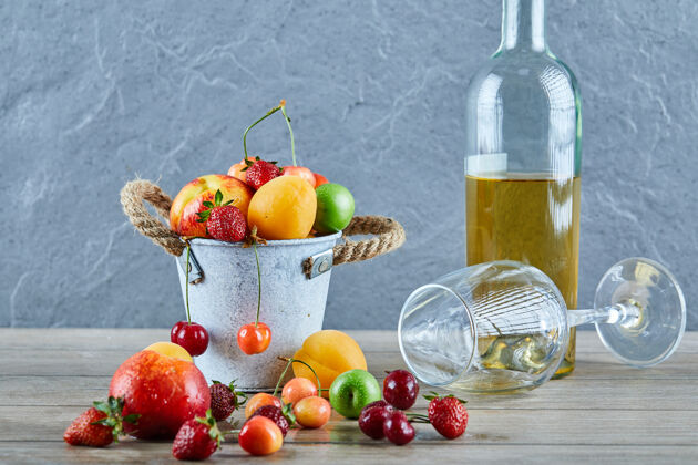 景观木桌上有一桶夏天的新鲜水果 一瓶白葡萄酒和空杯子瓶子葡萄酒草莓