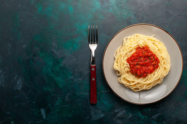 意大利面俯视图：深蓝色表面上有肉末和番茄酱的熟意大利面食意大利面午餐配料