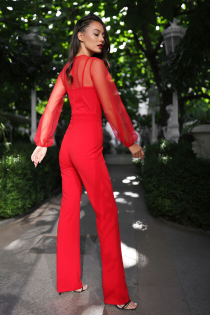 女性迷人的黑发女郎穿着红色西装站在花园里 发型 妆容 高跟鞋 鞋子 衬衫 裤子 亮丽 淑女 迷人 时尚户外微笑人