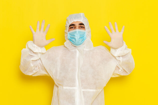 服装身穿特殊防护服 戴着面罩的男性科学工作者的正面图 双手放在淡黄色的墙上工人正面人