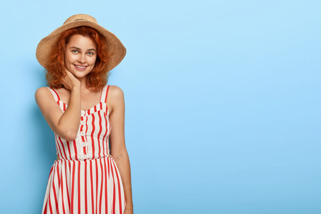 穿幸福的红发女人穿着时尚的夏装 戴着草帽 微笑迷人 自然美丽 靠着蓝色的墙壁 空白处为您宣传女人女士魅力