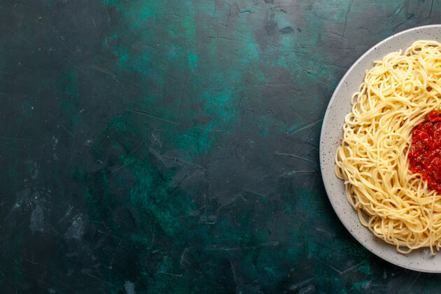 生的在深蓝色的桌子上可以俯瞰意大利面和肉末和番茄酱烹饪意大利晚餐