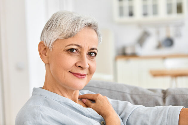 退休室内特写照片：优雅的退休老人在家里放松 淋浴后舒适地坐在沙发上 穿着舒适的棉质浴袍 带着可爱迷人的微笑肖像老年优雅