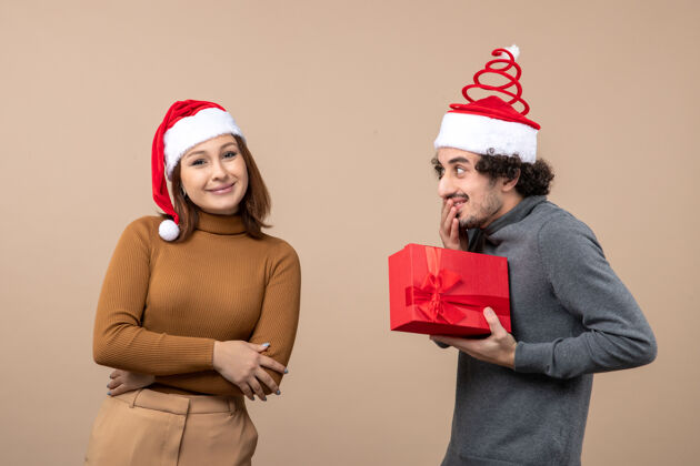圣诞老人新年气氛喜庆的概念与有趣可爱的情侣戴着红色圣诞老人帽女孩送他的礼物就灰色圣诞节可爱的情侣帽子