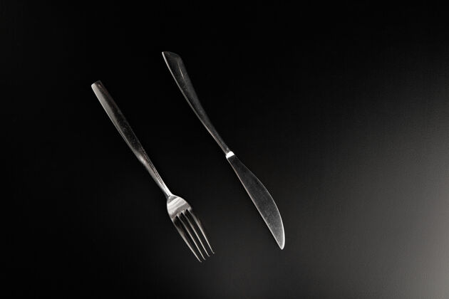 菜优雅的不锈钢刀叉放在光滑的黑色桌子上 面对着观众 彼此平行晚餐清洁器具