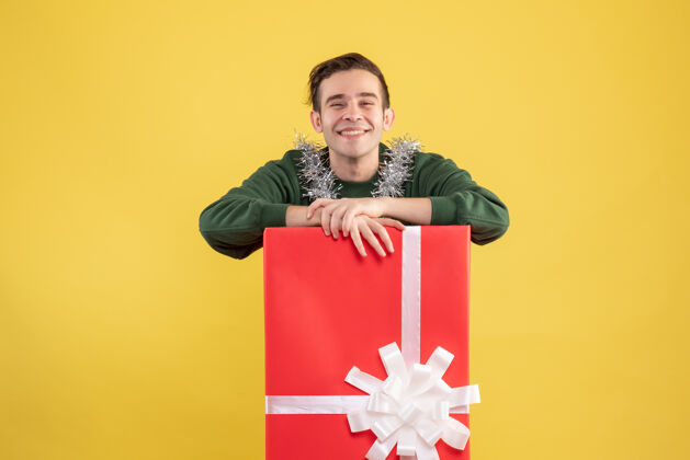 英俊正面图：站在黄色大礼盒后面的笑嘻嘻的年轻人大笑礼品盒年轻人