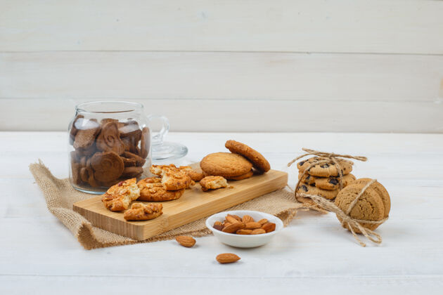 曲奇一些棕色的饼干和杏仁放在碗里 饼干放在砧板上 还有一个装在白色表面玻璃罐里的袋子杏仁烘焙玻璃