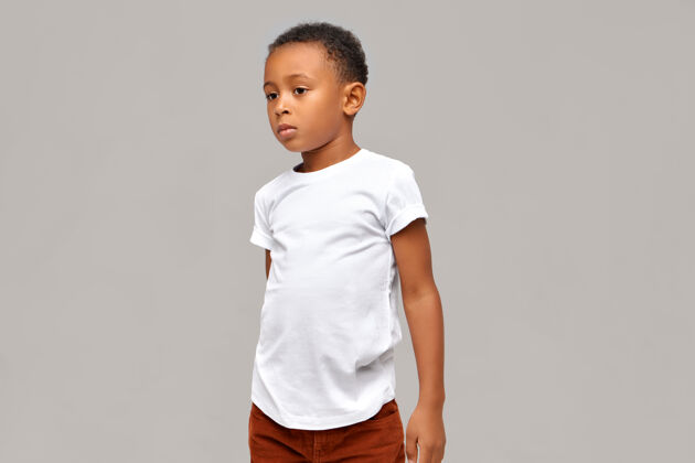 肖像半侧面的照片 穿着休闲的非洲男孩在白色t恤有冷静自信的面部表情摆在空白的墙壁与复制空间为您的信息隔离孩子种族小