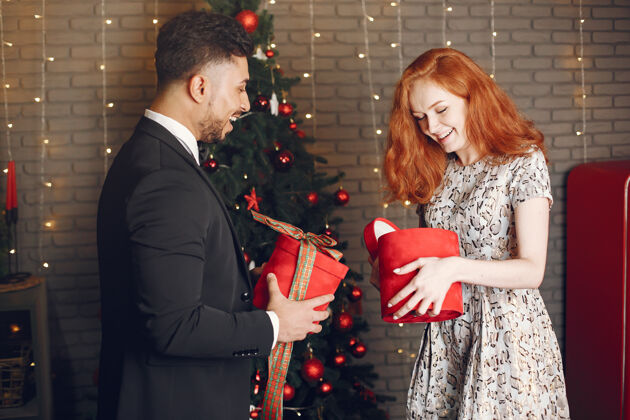 欢乐穿圣诞装饰品的人穿黑色西装的男人穿红色盒子的女人乐趣快乐成人