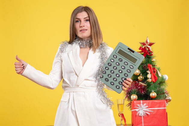背景正面图女医生站着拿着计算器 背景是黄色的圣诞树和礼品盒主任人举行