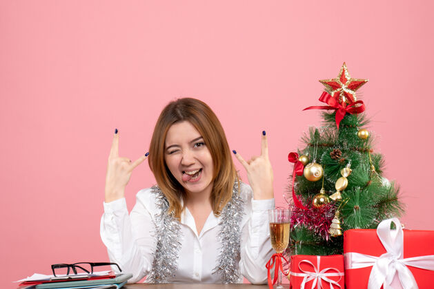 工作女工人坐在桌子后面 拿着礼物摆在粉红色的桌子上圣诞节礼物摆姿势